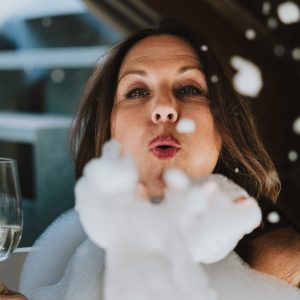 Frau pustet Seifenblasen vom Badeschaum in der freistehenden Badewanne in stylischem Apartment der H5 Studios by Hotel Grauer Bär Innsbruck.
