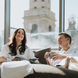 Paar entspannt auf Liegen mit Blick auf Innsbruck im Wellnessbereich des Partnerhotels Grauer Bär Innsbruck, bei Buchung der H5 Studios.