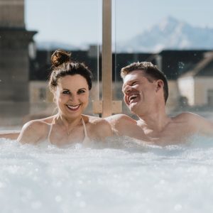 Pärchen relaxt im Outdoor-Whirlpool mit Bergblick im Wellnessbereich des Partnerhotels Grauer Bär Innsbruck, während sie in den H5 Studios wohnen.